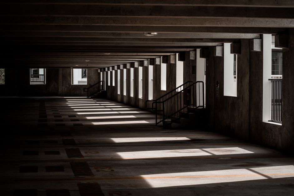 Dim concrete parking deck with bands of sunlight falling across the floor through side openings.