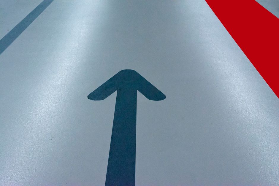 Blue arrow and red line on a parking garage floor signify direction and order.